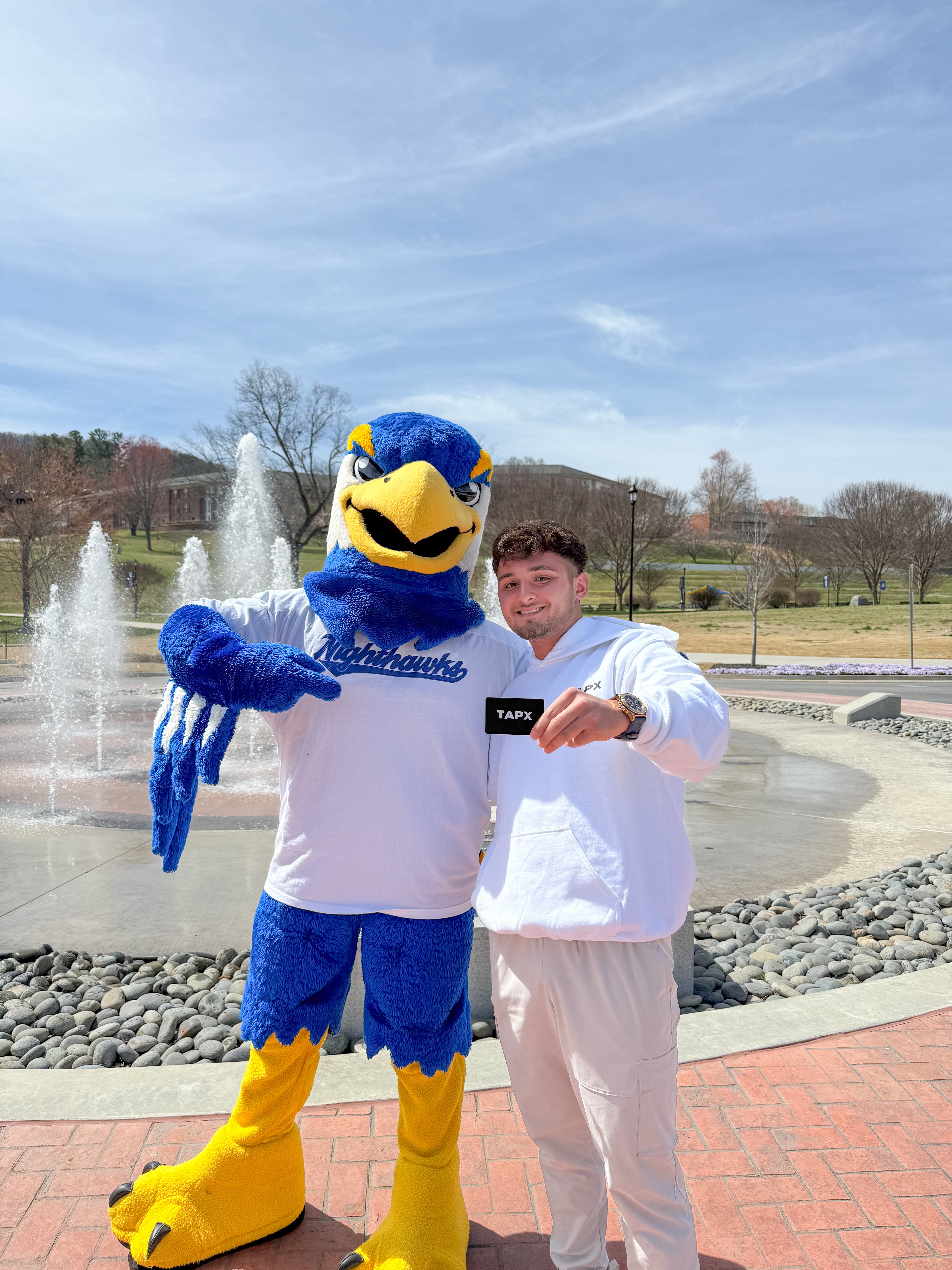 University of North Georgia Nighthawk mascot with student showcasing TapX card at campus fountain